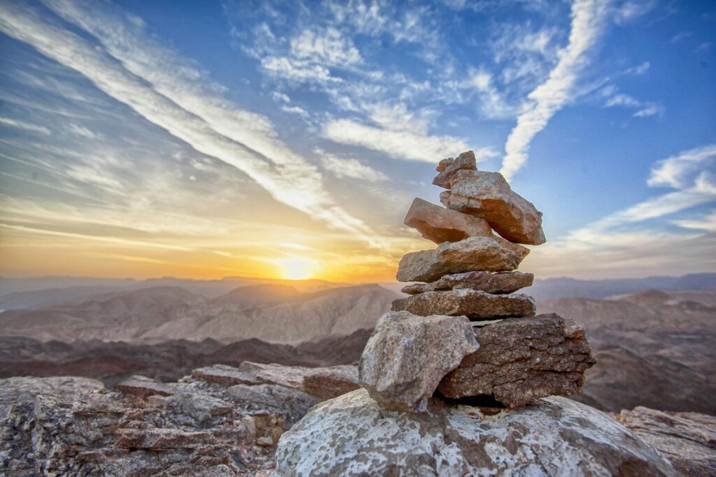 Stacked stones atop a mountain at sunset, with a breathtaking sky and landscape in the background.