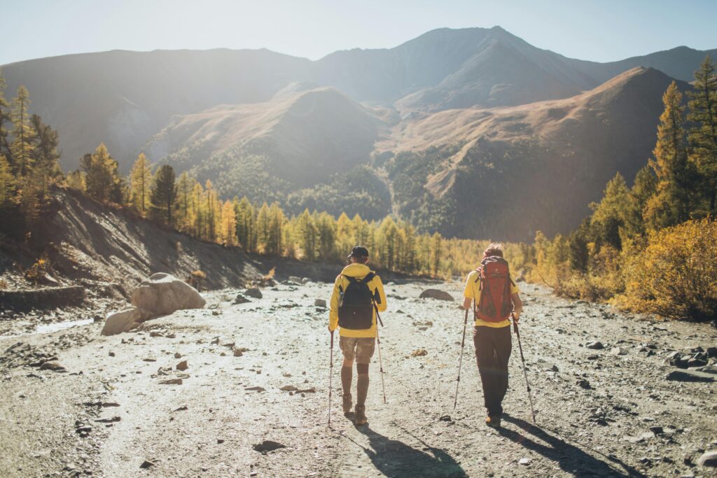 Two hikers exploring a scenic mountain trail during autumn with backpacks and walking sticks.