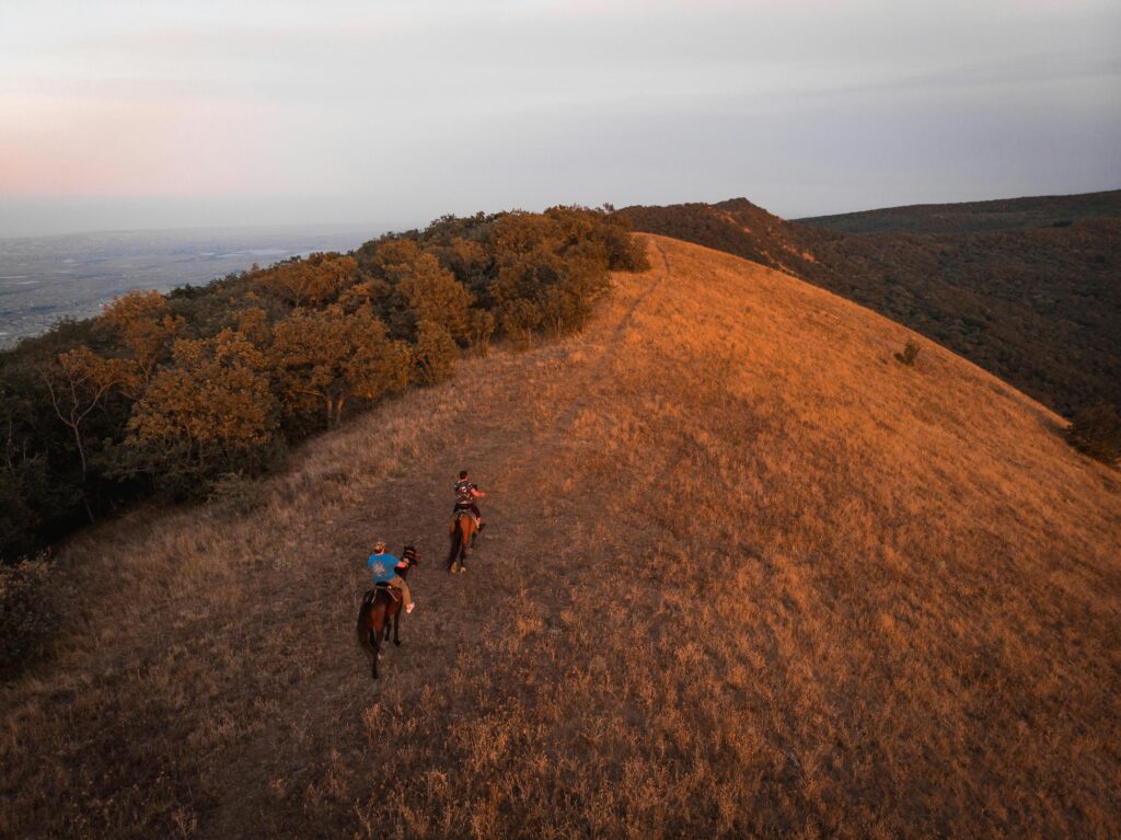 Two horseback riders traverse a scenic ridge in Dagestan, Russia during golden hour.