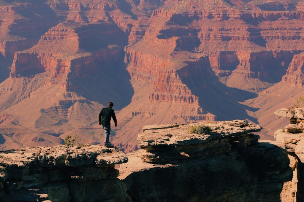 Person walking along the rim of the Grand Canyon with sweeping views of layered red rock cliffs and deep canyons below