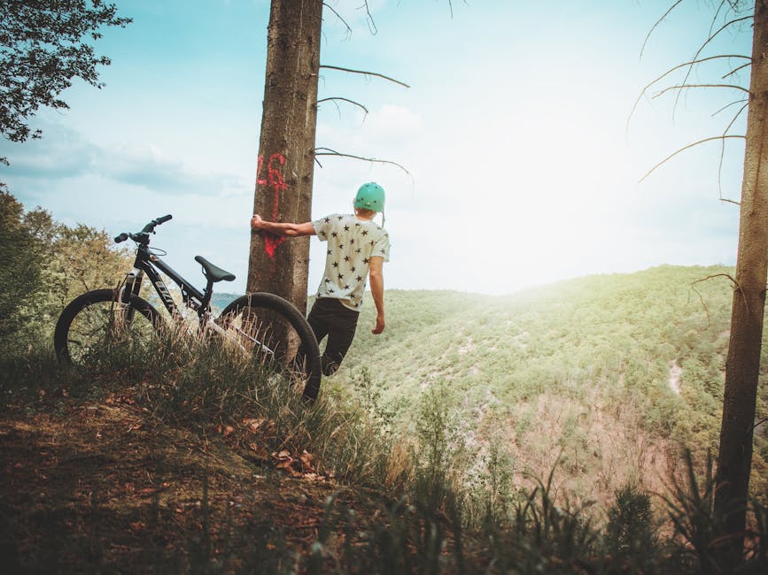 Teenager with bike on a mountaintop, enjoying the scenic landscape and summer freedom.
