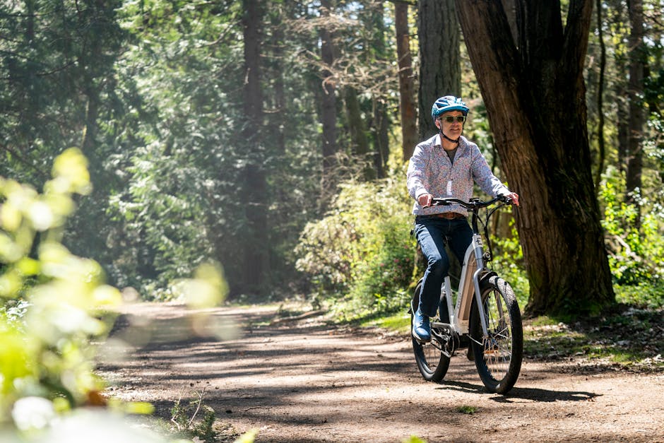 A man riding an e-bike through a forest path in Seattle, wearing a helmet and sunglasses.