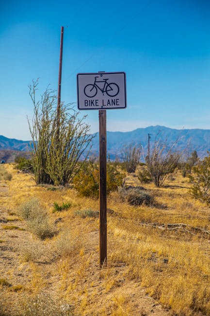 Bike lane sign post in a desert landscape with mountains in the background, indicating cycling path.