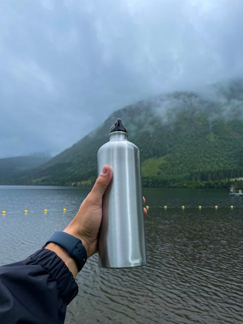 A metal bottle is held in front of a picturesque lake in Volda, Norway.