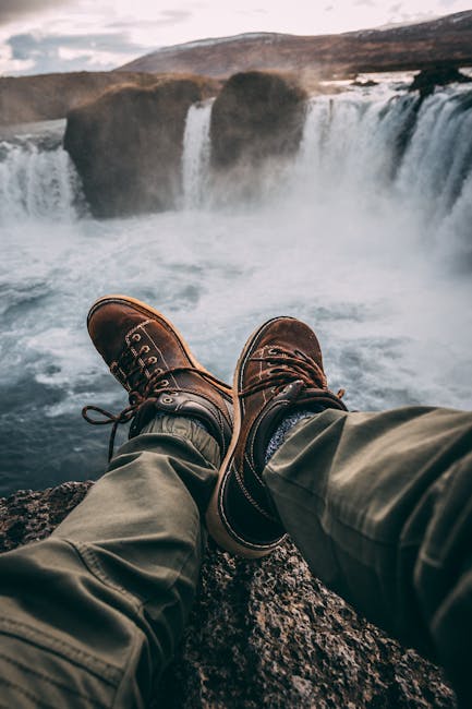 Person in hiking boots sitting at cliff's edge, overlooking breathtaking waterfall.