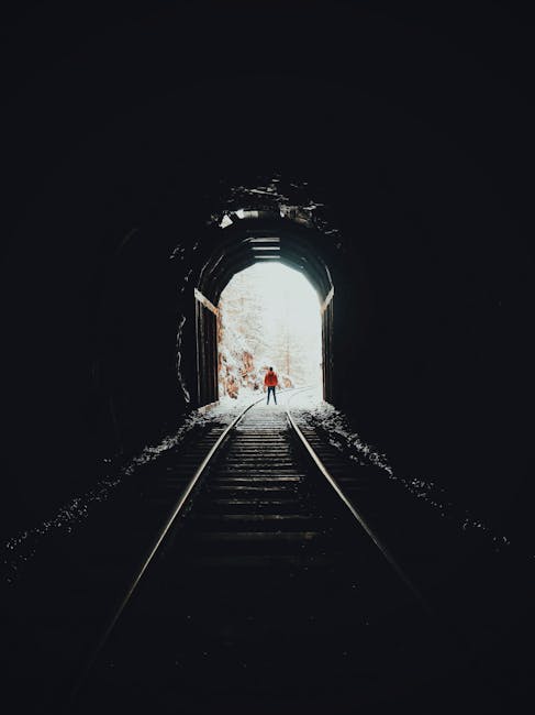 A lone figure stands at the end of a dark railway tunnel, creating a striking silhouette.