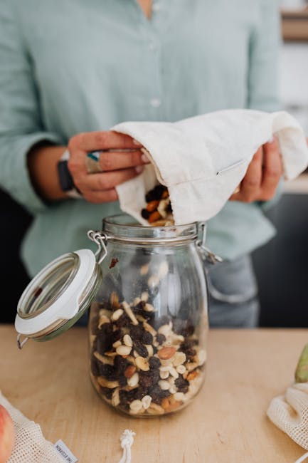Close-up of a woman pouring homemade trail mix into a glass jar, promoting a zero-waste lifestyle.