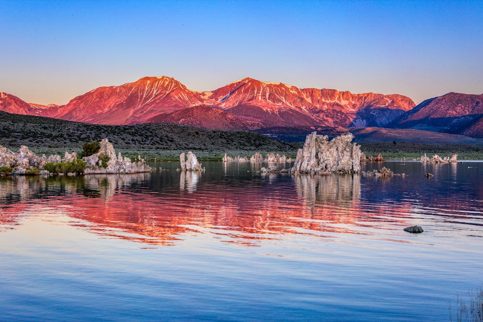 Stunning sunrise view of tufa formations reflecting in Mono Lake, California, with mountains in the background.