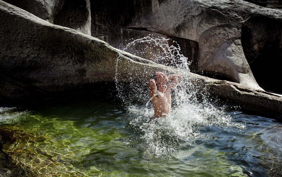 An adult man joyfully splashing water in a natural rock pool, creating a splash. Perfect summer outdoor activity image.