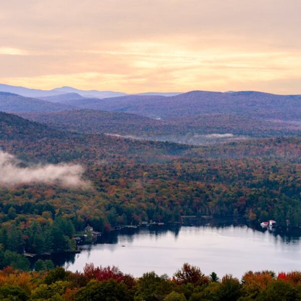 Breathtaking view of Adirondack Mountains with vibrant autumn colors at sunrise over a serene lake.