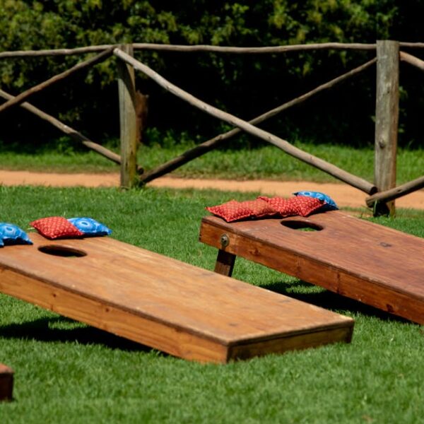 Wooden cornhole boards with colorful bean bags on a green lawn during a sunny day outdoors.