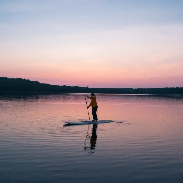 A serene scene of a person paddleboarding on a tranquil lake during sunset, reflecting golden hues.